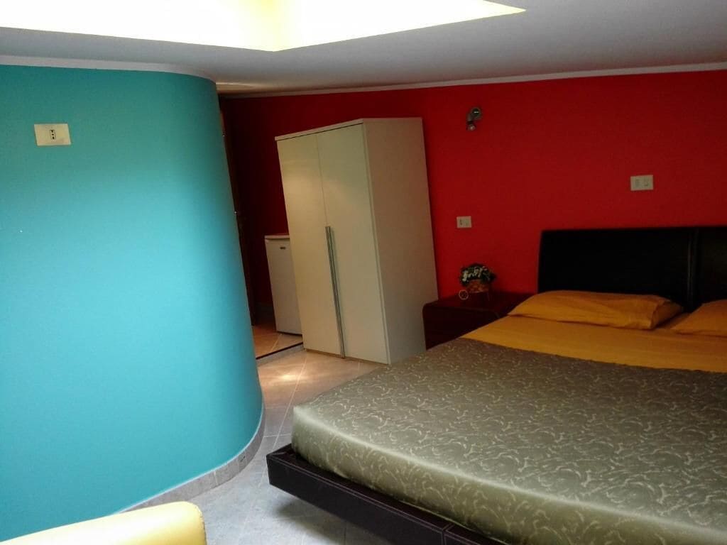 A bedroom with a bed, a wardrobe, and a small table with a lamp.
