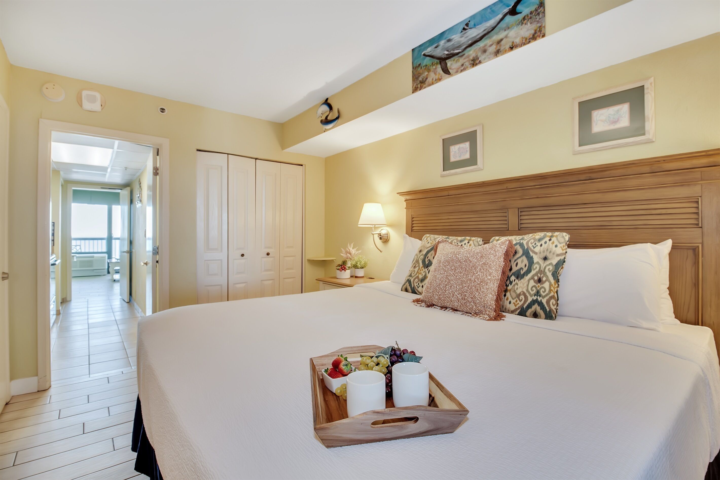 Une chambre d’hôtel avec un grand lit, une table de chevet avec une lampe et un plateau avec des fruits et des verres.