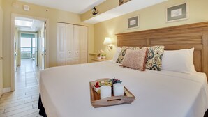A hotel room with a large bed, a bedside table with a lamp, and a tray with fruits and glasses. - Coastal Chic 1BR Oceanfront Suite (Myrtle Beach)
