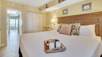 Une chambre d’hôtel avec un grand lit, une table de chevet avec une lampe et un plateau avec des fruits et des verres.