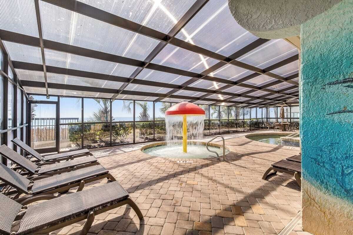 Un espace piscine extérieur abrité, doté de chaises longues, d’un élément décoratif central avec de l’eau et offrant une vue sur le paysage environnant.
