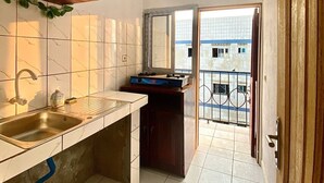 A compact kitchen with a sink, cabinets, and a window overlooking a balcony. - MyFurnishedYassa_Yatchika (Douala)
