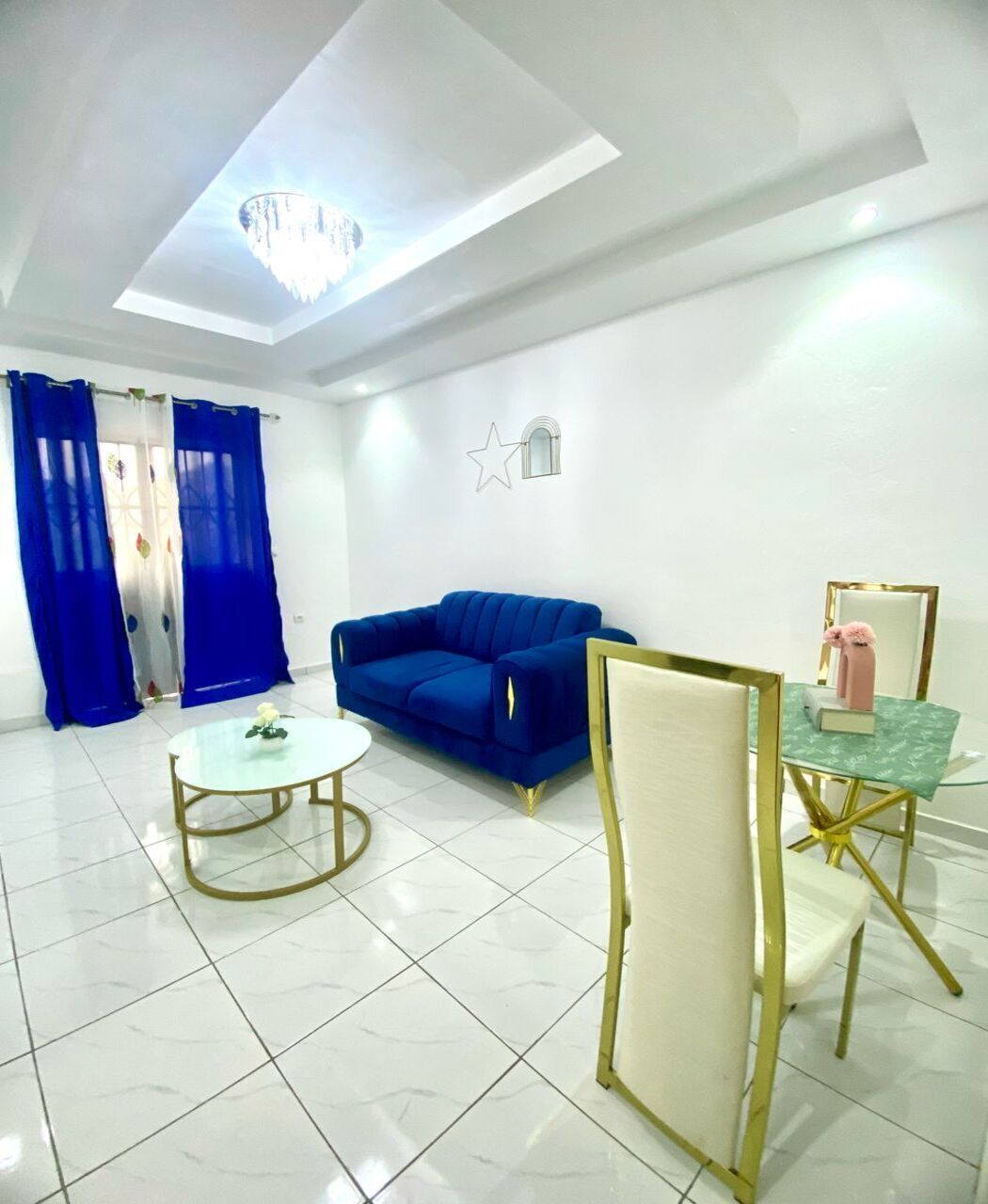 A modern living room with a blue sofa, a glass coffee table, and a small side table with a pink vase.