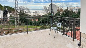 Ein Balkon mit Metallgeländer, einer Satellitenschüssel und einem Stuhl.