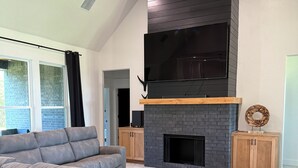 Ein modernes Wohnzimmer mit einem Ecksofa, einem Kamin und einem großen Fernseher, der darüber angebracht ist.