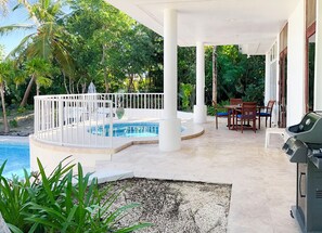 A covered outdoor area with a pool, seating, and a grill. - Canal-Front Villa in a Tropical Paradise in Leeward Settlement! (Leeward Settlement)