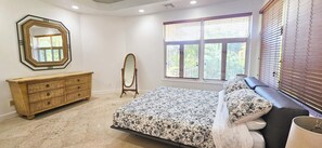 A bedroom with a bed, dresser, vanity, and a large window with blinds. - Canal-Front Villa in a Tropical Paradise in Leeward Settlement! (Leeward Settlement)