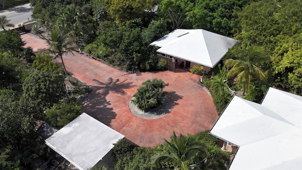 An aerial view of a residential area with a paved driveway, a circular garden with a palm tree, and a house with a white roof. - Canal-Front Villa in a Tropical Paradise in Leeward Settlement! (Leeward Settlement)