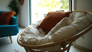 A wicker chair with a white and brown cushion, positioned near a window with a view of trees. - Les Ondines - T3, Parking, Garden & Near center. (Collioure)