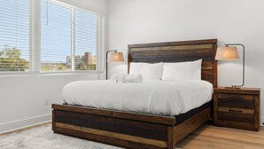 Un dormitorio con una cama de madera, ropa de cama blanca, dos lámparas de noche y vistas amplias a través de grandes ventanales.