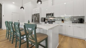 Una cocina moderna con armarios blancos, una isla central y un área de comedor con sillas verdes.