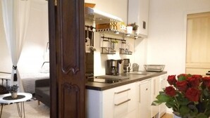 A compact kitchen with white cabinets, a black countertop, and a hanging pot rack. - Charming 26m2 studio in the center, 50m from the thermal baths (Bagnères-de-Bigorre)
