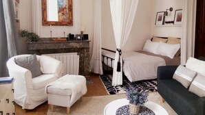 A modern bedroom with a bed, a sitting area with a chair and ottoman, a fireplace, and a large mirror. - Charming 26m2 studio in the center, 50m from the thermal baths (Bagnères-de-Bigorre)
