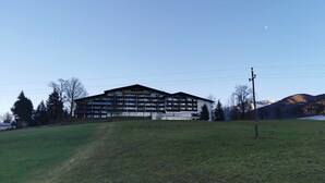 En stor, mangeetagers bygning med fladt tag, sandsynligvis et hotel eller resort, beliggende på en græsklædt bakke under en klar himmel.