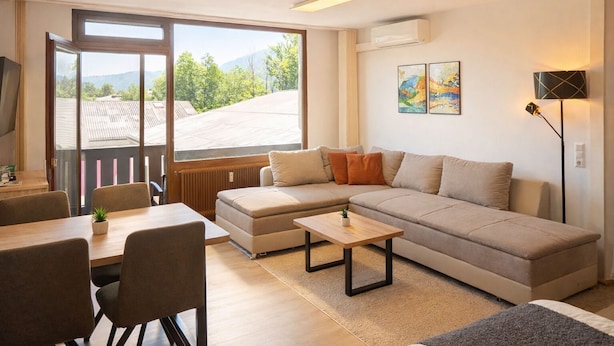 En moderne stue med sofa, sofabord og spiseområde. Der er et stort vindue med udsigt til det fri.