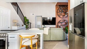 Uma cozinha moderna com área de refeições, uma sala de estar com sofá e TV, e uma escada.
