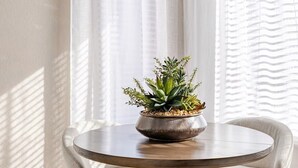 Uma área de jantar com uma mesa redonda, quatro cadeiras, uma luminária pendente geométrica e um arranjo de plantas.