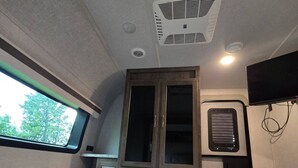Interno di un camper compatto con un letto, un angolo cottura, una finestra e una TV a parete.