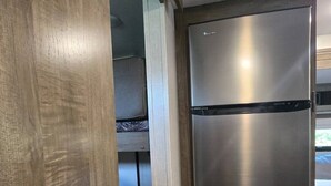 Una cucina compatta con un frigorifero in acciaio inox, una porta in legno e un piccolo angolo relax con un cuscino a righe.