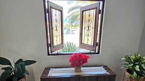 Ein Holzkonsolentisch mit einem gewebten Korb auf jeder Seite, einer Vase mit roten Blumen und einem Fenster mit geöffneten Rollläden.