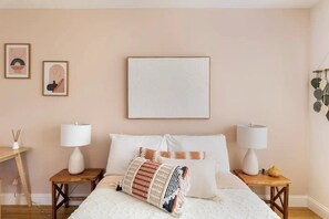 Une chambre à coucher avec un lit, deux tables de chevet avec des lampes et deux œuvres d’art encadrées accrochées au mur.