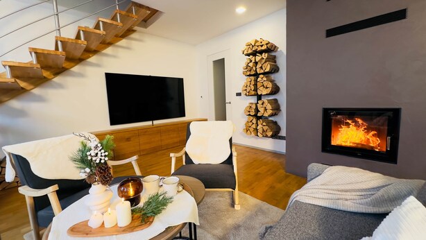 A modern living room with a staircase, a fireplace, a television, and a dining area with candles and a decorative centerpiece.