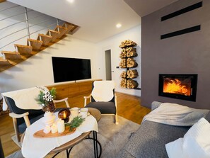 Un soggiorno moderno con una scala, un camino, una televisione e un'area pranzo con candele e un elemento decorativo.