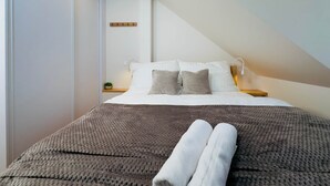 A modern bedroom with a large bed, a bedside table, a lamp, and a small plant.