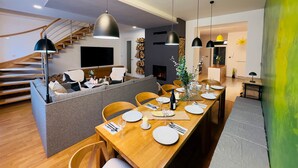 A modern dining area with a long wooden table set for a meal, a staircase with wooden steps, and a flat-screen TV mounted on the wall.