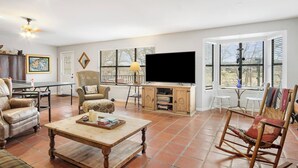 Ein geräumiges Wohnzimmer mit Fernseher, bequemen Sitzgelegenheiten und großen Fenstern.
