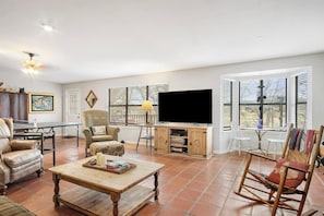 A spacious living room with a flat-screen TV, comfortable seating, and large windows. - Guadalupe Getaway | Riverfront | Close to Town (Kerrville)