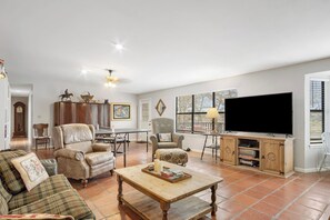 A spacious living room with a large flat-screen TV, leather armchairs, a wooden coffee table, and a dining area with a chandelier. - Guadalupe Getaway | Riverfront | Close to Town (Kerrville)