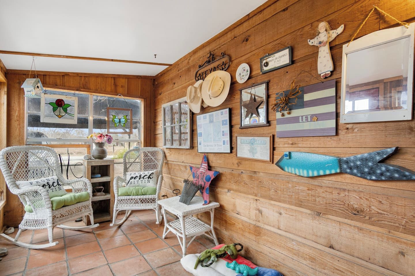 Ein gemütliches Zimmer mit Holzwänden, Korbmöbeln und verschiedenen Wanddekorationen, darunter gerahmte Bilder und eine Meerstern-Verzierung.