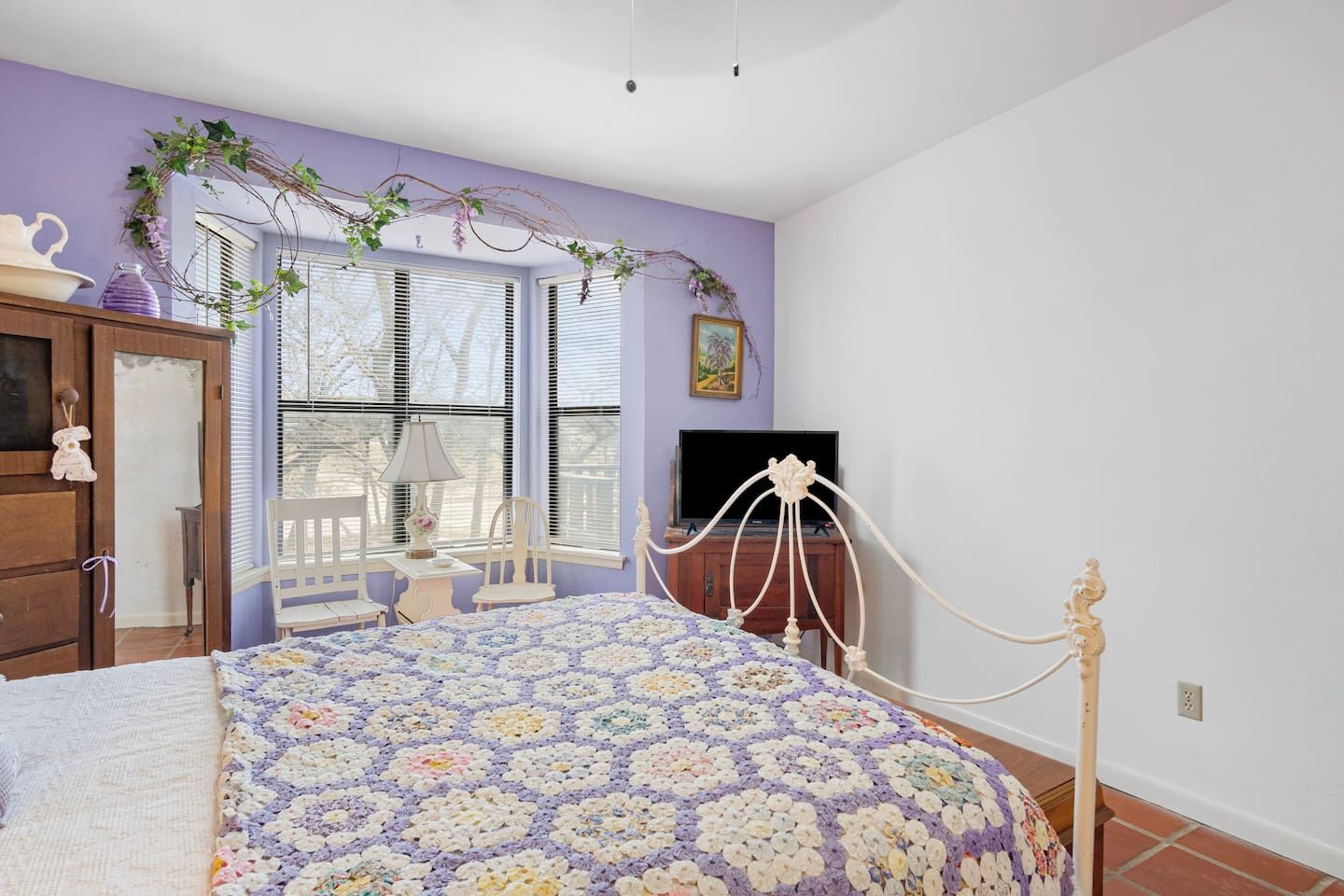 A bedroom with a bed, a dresser, a television, and a window with blinds.