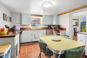A compact kitchen with a dining area, featuring light-colored cabinets, a window with blinds, and a tiled floor. - Guadalupe Getaway | Riverfront | Close to Town (Kerrville)