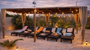 A covered outdoor seating area with lounge chairs and string lights. - Apartments Diva "Flamingo" (Barber)