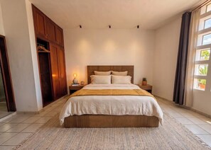 Ein Schlafzimmer mit einem großen Bett, einem Holzschrank, Nachttischlampen und einer Topfpflanze.