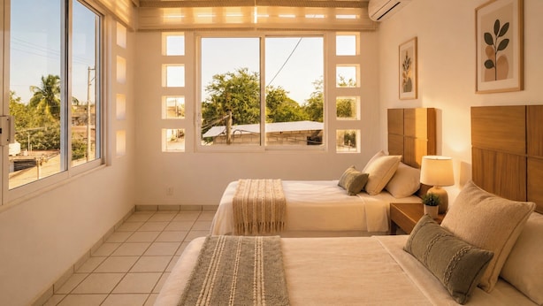 Un dormitorio con dos camas, un ventanal y vistas al verdor exterior.