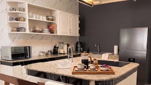 Una cocina moderna con encimera de granito, armarios blancos, microondas integrado, cafetera y refrigerador de acero inoxidable.