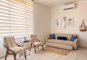 A living room with a sofa, two chairs, a small table with a plant, and a rug.