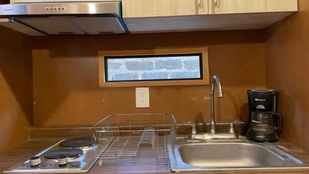 Una cocina compacta con estufa de acero inoxidable, un lavamanos y una cafetera.