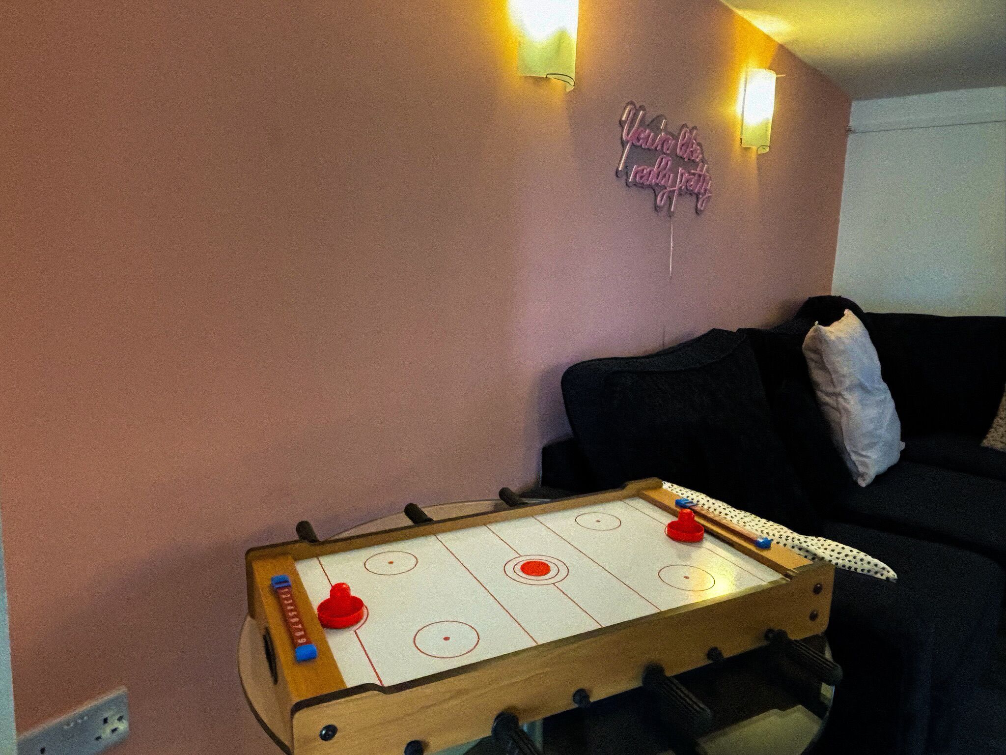 Una habitación con una mesa de futbolín, un sofá negro y un cartel en la pared.