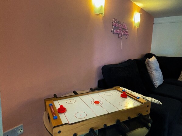 Una habitación con una mesa de futbolín, un sofá negro y un cartel en la pared.