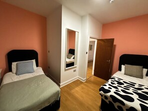 Quarto com duas camas, um espelho e uma porta que dá para outro cômodo.