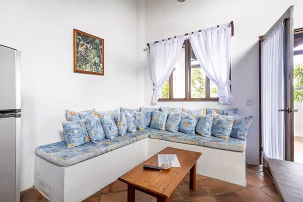 Une pièce comprenant un canapé, une table en bois, une fenêtre avec des rideaux et un tableau accroché au mur.