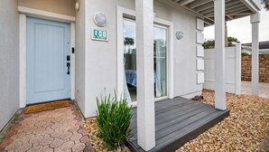 A house with a light blue door, a small porch with a wooden deck, and a white exterior wall. - Steps to Beach & Ocean View | Good Morning Rentals (Jacksonville Beach)