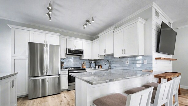 A modern kitchen with white cabinets, stainless steel appliances, a marble island, and bar stools. - Steps to Beach & Ocean View | Good Morning Rentals (Jacksonville Beach)
