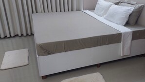 Siististi pedattu sänky, jossa on valkoinen patja ja beigenvärinen päällinen, valkoinen tyyny ja valkoinen peitto.