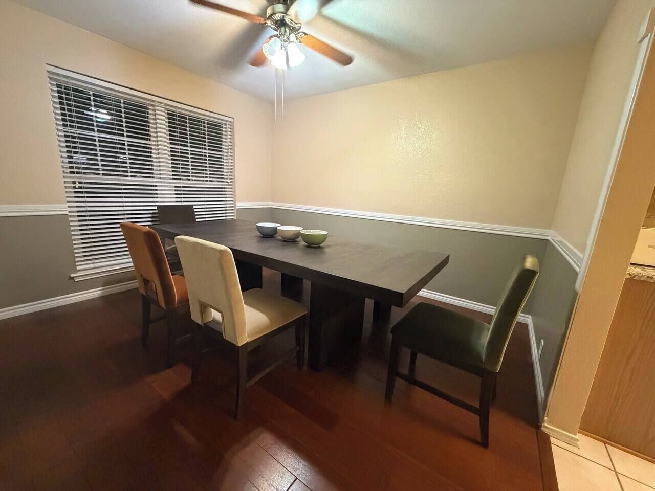 A dining room with a dark wooden table, four chairs, and a ceiling fan.