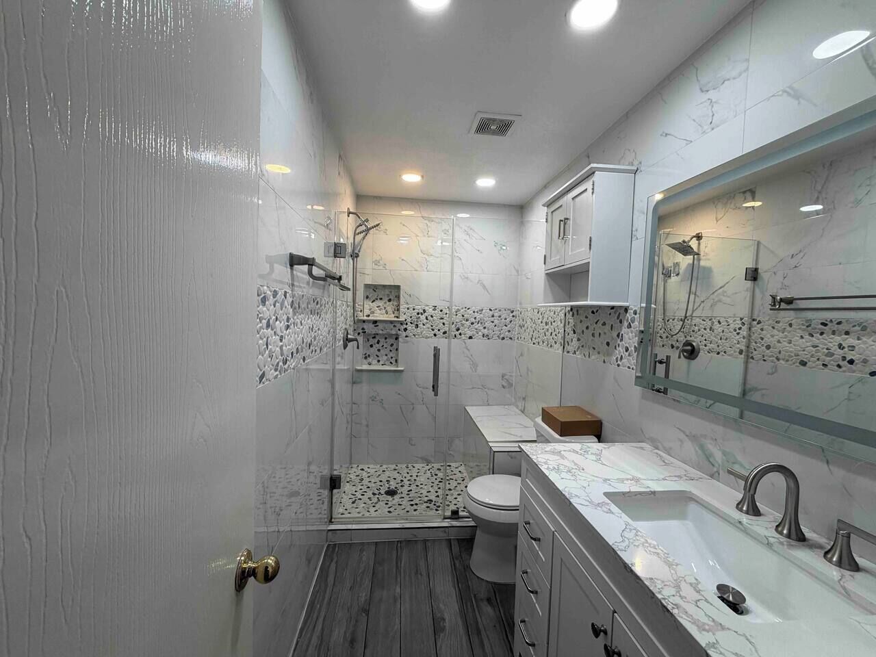 A modern bathroom with a shower, toilet, and sink, featuring marble tiles and a large mirror.